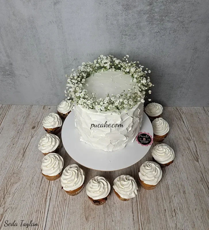 Beyaz çiçeklerle süslenmiş pasta ve beyaz kremalı cupcakeler