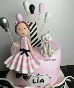 Kız ve kedi figürleri, balonlar ve siyah beyaz fiyonkla süslenmiş iki katlı pembe 1 yaş pastası